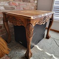 Close-up photo showing one side of a floral carved wooden side table with curved legs ending in claw feet and intricate floral design on leg and apron.