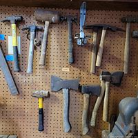 Hammers and mallets mounted on pegboard displaying wide variety including claw hammers, mallet, axes and sledgehammers.