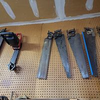 Image showing electric chain saw and five vintage handsaws with wooden handles on pegboard wall.