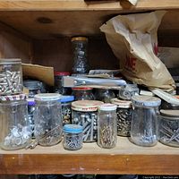 Shelf with assorted hardware items including jars of screws, nails, and metal fasteners