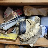Shelf showing a cluttered mix of old hand tools including a dirty glove, metal parts, and various small boxed items.