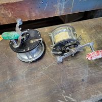 Three Penn brand fishing reels with varying handle colors and sizes, some loaded with fishing line, arranged on a wooden surface