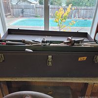 Front view of black metal toolbox with lid open showing hand tools inside