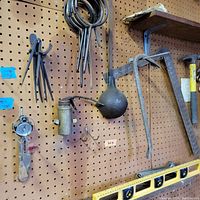 Tools hanging on pegboard featuring calipers, hooks, oil can, hammer, crowbar, and spirit level
