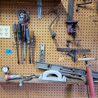 Vintage hand tools hanging on pegboard including screwdrivers, a hand saw, clamps, levels, and a hand plane