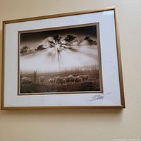 Framed black and white photograph of a sheepherder with sheep and sun rays shining through trees.