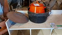 Photo showing two cast iron pots: a large black one with lid and handle, and an orange enamel pot inside it.