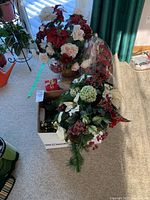 Overview of the lot with faux flower arrangements and other decoration items on carpet near window.