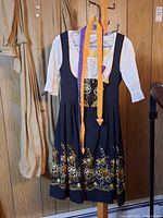 Full view of the navy blue dirndl dress with white blouse underneath and colorful ribbons hanging.