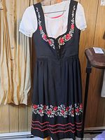 Full length view of black dirndl dress with floral embroidery and white blouse hanging on hanger