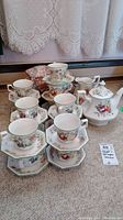 Group photo of 13 cups and saucers, teapot, and pitcher arranged on carpeted floor.