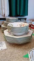 Stack showing various octagonal plates including side, salad, dinner plates and cereal bowls with a multicolor fruit pattern and green rim.