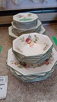 Stack of bowls and plates featuring fruit and floral design with green rim.