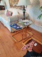 Nesting tables set of three with gold metal frames and glass tops beside couch and lamp.