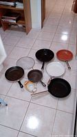 Image showing 6 pans, metal splatter screen, and silicone Poachie in packaging arranged on floor.