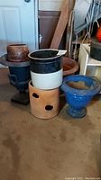 Group photo showing assorted plant pots including a black and white crockery pot, terracotta pots with holes, and the blue ceramic pedestal pot.