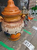 Photo showing the front side of the ceramic rum pot with lid, detailing the hand-painted fruit and embossed 'Rumtopf' lettering.