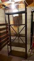 Full view of the assembled metal shelving unit in a basement setting, showing five shelves and cross-bracing for stability.
