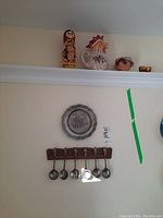 Wide shot showing wall plate, 6 spoons on rack, wooden Matroska doll, rooster pitcher, small bowl, and egg holders.