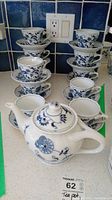 Full set showing teapot in front with stacks of teacups and saucers behind on white countertop.