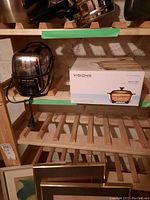 General Electric chrome toaster and Visions cookware box on wooden shelf in storage.