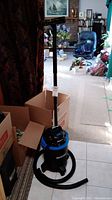 Full view of the Mastervac wet/dry vacuum cleaner with the hose coiled and tall handle attachment upright, standing on the floor next to boxes.