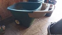 Full side view of the green plastic wheelbarrow showing the overall shape, handles, and wheels.
