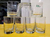 Photo of 7 clear glass drinking glasses: 4 round small glasses on bottom, 3 short circular glasses with square solid bases stacked on top.