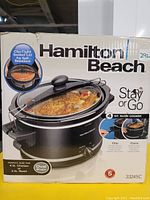 Boxed Hamilton Beach Stay or Go 4 Qt Slow Cooker featuring clip-tight sealed lid and an image of slow cooker with cooked food.