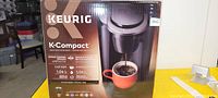 Photo of boxed Keurig K-Compact coffee maker showing brand, model, and image of the machine brewing coffee.