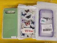 Photo showing three phone cases: a light green case for Google Pixel 6, a transparent butterfly patterned case labeled XS Max, and a translucent purple 'ownest' case for iPhone 11.
