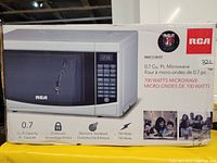Photo of box packaging showing RCA 0.7 cu. ft. microwave model RMW733 in white with 700 watts power, electronic touchpad and child lock features.