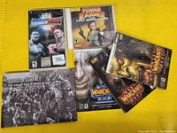 Photo showing five items including SmackDown RAW 2006 PSP game, Tomb Raider Last Revelation PC game, two Warcraft III CDs, and a French Warcraft-themed booklet.