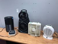 Wide view of all lot items showing air cleaner, three fans, and label maker on wooden table.