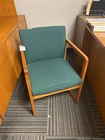 Front view of green upholstered armchair with wooden frame, showing seat, backrest, and armrests.