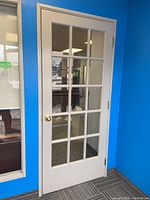 Photo of front side of wood door showing glass pane grid and brass door knob against blue wall background.