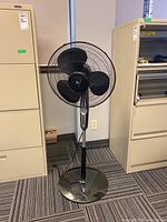 Full front view of the Weatherworks black standing fan, showing blades, protective grille, and base.