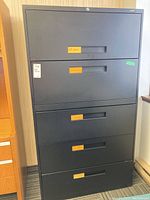 Front view of the black metal five drawer file cabinet with labels on each drawer and a visible lock on the top drawer.