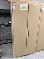 Front view of beige 2-door metal file cabinet with labels and scratches.