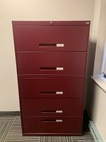 Front view of maroon metal filing cabinet with five drawers, including lock on top drawer.