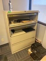 Front angle of beige metal filing cabinet with drawers open, showing contents not included.