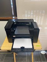 Front view of HP LaserJet P1606dn printer showing front paper input tray loaded with paper and top output tray with paper.