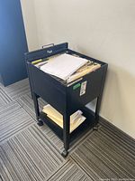 Side view showing the cabinet holding manilla file folders and stacks of papers on top and lower shelf with casters.