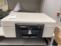Closed view of beige SentrySafe 1160 security safe with black locking handle and keyhole in front.
