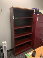 Frontal view of the shelving unit showing the four adjustable shelves and bottom shelf with reddish-brown wood veneer finish, black back panel, and light wood top surface.