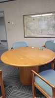 Image showing the round wood table from above, with three chairs around it, set in an office environment.