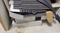 Three boxes stacked with commercial carpet remnants in grey and black strips.