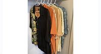 Six shirts hanging on hangers in a closet showing front view of all colors and prints.