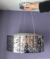 Hand adjusting circular metallic crystal nest pendant light suspended from ceiling by cables.