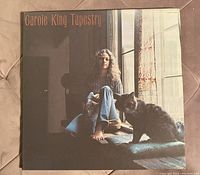 Front cover of Carole King Tapestry album showing Carole King sitting barefoot by a window with a cat.